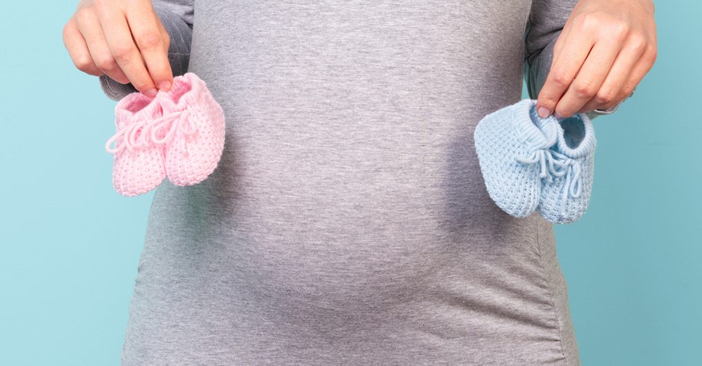 Pregnant woman holding baby booties - Busy Mommy Media